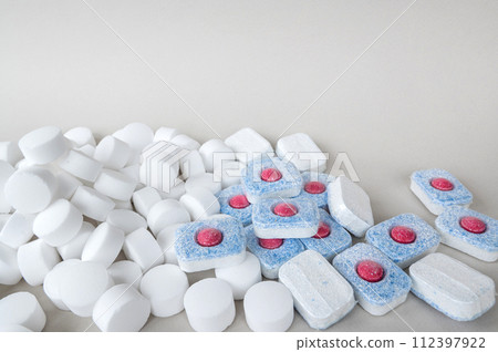 White pressed salt tablets and colored capsules with a red middle for a dishwasher close-up. White pressed salt tablets and colored capsules with a red middle for a dishwasher close-up. 112397922