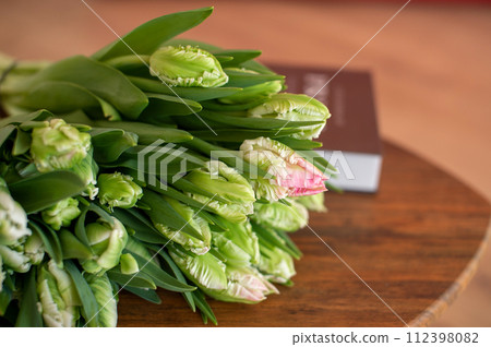 Green and pink parrot tulips on wooden table with book. 112398082
