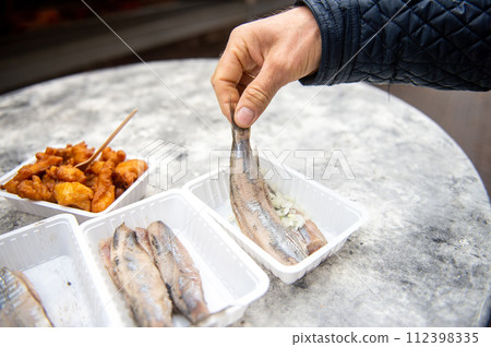 The Netherlands, Delft 2022. Food from a fish restaurant, . Hold herring with onions by the tail. 112398335