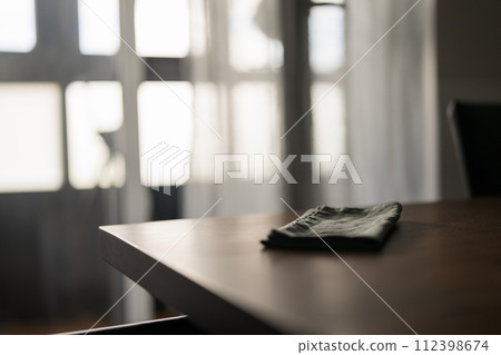 Dark green linen napkin on walnut table indoor with natural window light 112398674