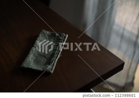 Dark green linen napkin on walnut table indoor with natural window light Dark green linen napkin on walnut table indoor with natural window light 112398681