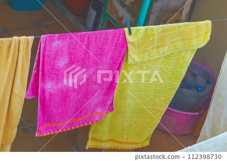 Colorful clothes after washing are hung on a clothesline to dry in the wind, pink, yellow towels. Household hygiene items 112398730