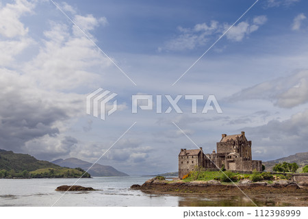 Storied Eilean Donan Castle presides over a loch against lush Highland greenery under expansive sky Storied Eilean Donan Castle presides over a loch against lush Highland greenery under expansive sky 112398999