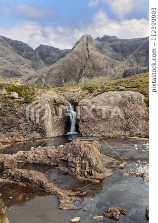 Skye's Fairy Pools invite with calm waters and mountainous backdrop, showcasing wild beauty 112399003