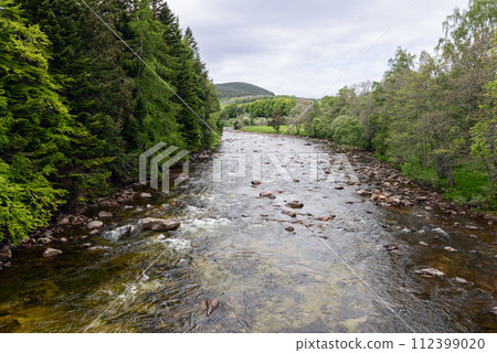 Serene river meanders through vibrant green Scottish forests, with hills on the horizon Serene river meanders through vibrant green Scottish forests, with hills on the horizon 112399020