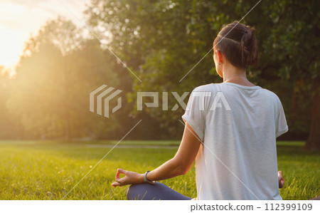Young asian woman doing meditation in morning or evening at park, healthy woman relaxing and practicing yoga at city park. Mindfulness, destress, Healthy habits and balance concept 112399109