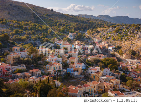 Symi Island, Greece. Greece islands holidays from Rhodos in Aegean Sea. Colorful neoclassical beautiful houses on hillsides of a Greek island during sunset. Holiday travel background. Symi Island, Greece. Greece islands holidays from Rhodos in Aegean Sea. Colorful neoclassical beautiful houses on hillsides of a Greek island during sunset. Holiday travel background. 112399113