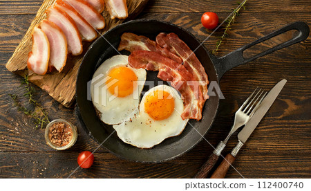 Bacon and Two Fried Eggs in a Black Skillet Top View - Generative Ai 112400740