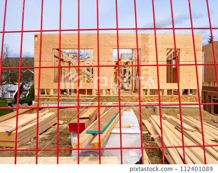 Wooden frame and walls of new house behind the red fence grid 112401089
