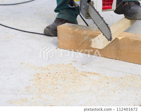 Worker sawing a wooden plank with a chainsaw 112401672