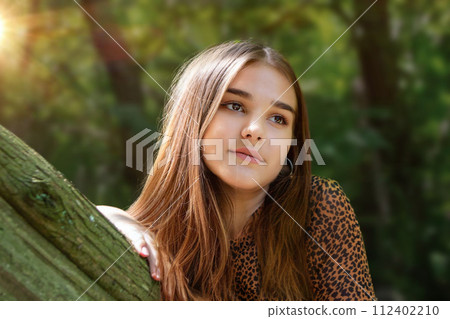 Emotional girl teenager with long hair hairstyle braids in a green shirt sits on a bench in the park. High quality photo 112402210