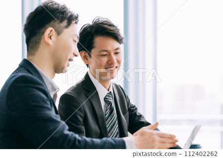 Two male businessmen talking while looking at a computer Two male businessmen talking while looking at a computer 112402262