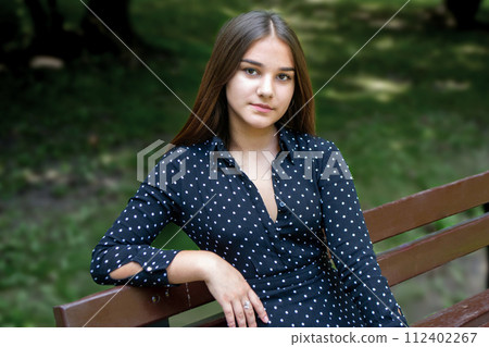 Emotional girl teenager with long hair hairstyle braids in a green shirt sits on a bench in the park. High quality photo 112402267