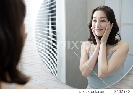 A woman puts her hands on her cheeks while looking in the mirror 112402580