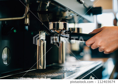 At restaurant or pub coffee machine brews fresh tasty coffee. Step by step guide to professional coffee making process. Close up of machine hand holding handle pouring espresso. At restaurant or pub coffee machine brews fresh tasty coffee. Step by step guide to professional coffee making process. Close up of machine hand holding handle pouring espresso. 112403674