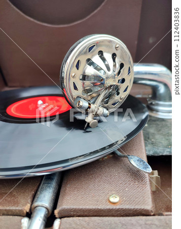 An old retro record playing on old vintage gramophone at flea market. Work of portable gramophone. Old vintage shabby record player, phonograph, potefone. Needle close up. Nostalgia antique turntable An old retro record playing on old vintage gramophone at flea market. Work of portable gramophone. Old vintage shabby record player, phonograph, potefone. Needle close up. Nostalgia antique turntable 112403836