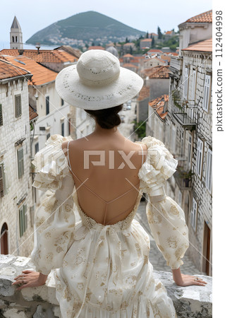 AI-generated content. A woman in a white gown and sun hat is standing on a balcony, overlooking the city below. The sleeve of her dress flutters in the wind as she enjoys the view AI-generated content. A woman in a white gown and sun hat is standing on a balcony, overlooking the city below. The sleeve of her dress flutters in the wind as she enjoys the view 112404998