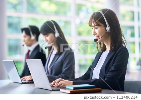 一位穿著西裝的女商人在辦公室裡戴著耳機並做出回應 112406214