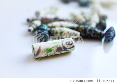 Handmade paper beads of brown, green, black colored floral patterns lying on white table side view Handmade paper beads of brown, green, black colored floral patterns lying on white table side view 112406243