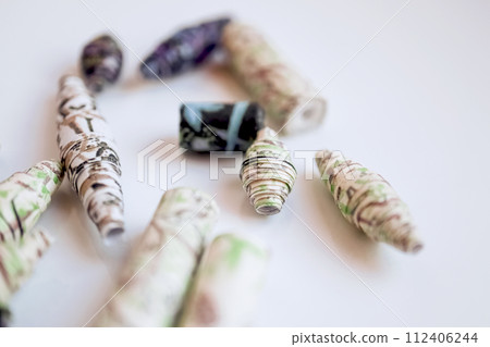 Handmade paper beads of brown, green, black colored floral patterns lying on white table side view Handmade paper beads of brown, green, black colored floral patterns lying on white table side view 112406244