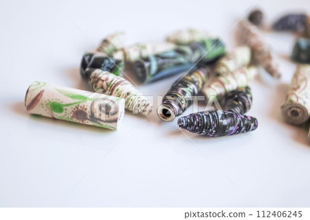 Handmade paper beads of brown, green, black colored floral patterns lying on white table side view Handmade paper beads of brown, green, black colored floral patterns lying on white table side view 112406245