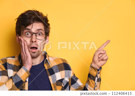 Funny amazed guy pointing at copy space on yellow studio background 112406415