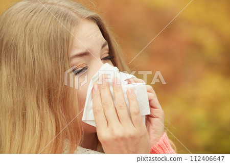 Sick ill woman in autumn park sneezing in tissue. Sick ill woman in autumn park sneezing in tissue. 112406647