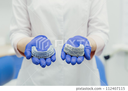 Woman working in dental clinic with patient sitting in chair and doctor in background. 112407115