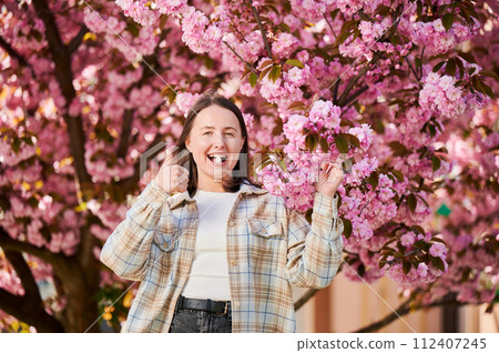 Woman allergic suffering from seasonal allergy at spring. Young happy woman applying allergy pill, giving thumbs up, posing in blossoming garden at springtime. Antihistamine medication concept 112407245