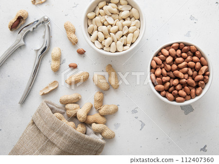 Whole and peeled peanut nuts with cracker and linen bag on light background. 112407360