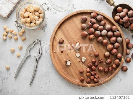 Wooden plate with whole and peeled hazelnut nuts with cracker and jar on light background. Wooden plate with whole and peeled hazelnut nuts with cracker and jar on light background. 112407361