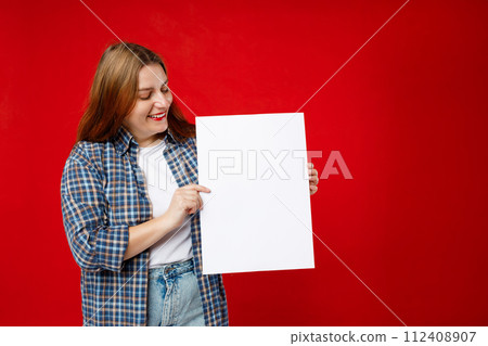 Beautiful 30s woman holding a blank advertisement banner isolated over red background. Young woman holding sign business board Beautiful 30s woman holding a blank advertisement banner isolated over red background. Young woman holding sign business board 112408907
