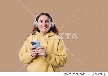 Beautiful young 30s woman wearing white wireless headphones and listening to music and using smart phone, girl isolated over colorful background wall 112408917