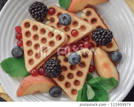 Homemade Belgian waffles served with fresh berries on white plate over wooden background, close up.  112409974