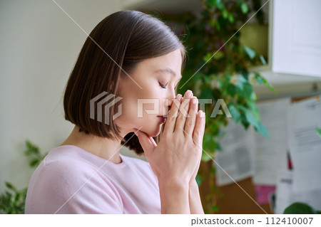 Profile view close-up of young woman's face with hands folded in prayer, dreams Profile view close-up of young woman's face with hands folded in prayer, dreams 112410007