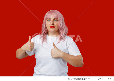 Young happy 30s Caucasian woman isolated on red background giving a thumbs up and good luck gesture, studio portrait. Young happy 30s Caucasian woman isolated on red background giving a thumbs up and good luck gesture, studio portrait. 112410056