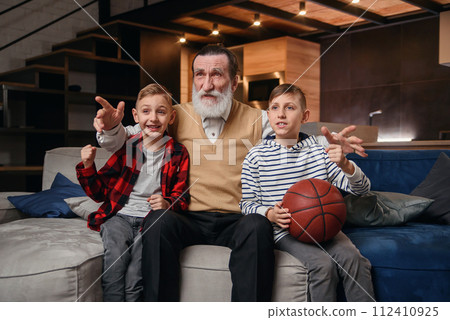 Boys on couch with their grandfather cheering for a basketball game and holding a basketball ball. Huge sports fanats. 112410925