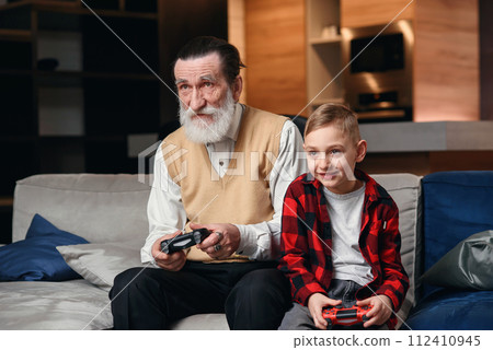 Cute little boy with grandfather sitting on sofa and playing video game with game pad 112410945