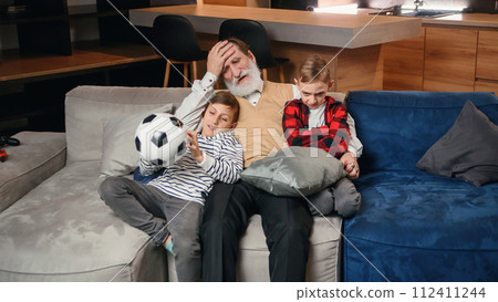 Excited three generations of men sport fans relax in living room celebrate team victory together, overjoyed little boy with dad and grandfather have fun watching football match at home together 112411244