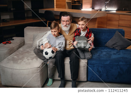 Excited three generations of men sport fans relax in living room celebrate team victory together, overjoyed little boy with dad and grandfather have fun watching football match at home together Excited three generations of men sport fans relax in living room celebrate team victory together, overjoyed little boy with dad and grandfather have fun watching football match at home together 112411245