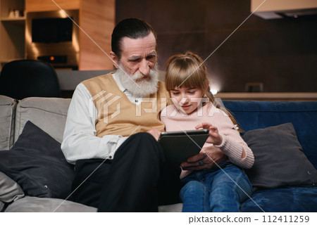 Grandfather with his granddaughter using tablet at home Grandfather with his granddaughter using tablet at home 112411259