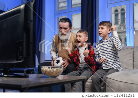 Likable concentrated senior bearded grandfather with his cheerful 10-15s grandsons spending their free time at revision the basketball game on tv Likable concentrated senior bearded grandfather with his cheerful 10-15s grandsons spending their free time at revision the basketball game on tv 112411281