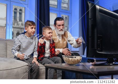 Likable concentrated senior bearded grandfather with his cheerful 10-15s grandsons spending their free time at revision the basketball game on tv Likable concentrated senior bearded grandfather with his cheerful 10-15s grandsons spending their free time at revision the basketball game on tv 112411282
