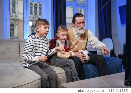 Likable concentrated senior bearded grandfather with his cheerful 10-15s grandsons spending their free time at revision the basketball game on tv Likable concentrated senior bearded grandfather with his cheerful 10-15s grandsons spending their free time at revision the basketball game on tv 112411285