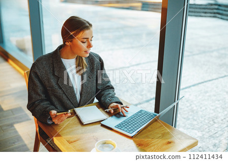 Business woman reading message on phone and work on laptop in cafe. Distance work concept Business woman reading message on phone and work on laptop in cafe. Distance work concept 112411434
