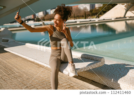 Portrait of sporty smiling young woman after running making selfie outdoors 112411460