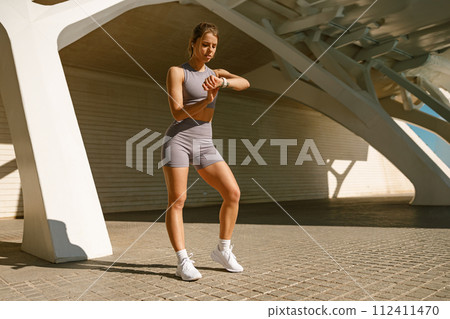 Young fit woman looking at smartwatch and counting calories burned. Healthy life concept Young fit woman looking at smartwatch and counting calories burned. Healthy life concept 112411470
