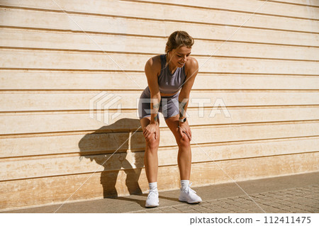 Smiling woman in sportswear have a rest after workout outside standing on wall background Smiling woman in sportswear have a rest after workout outside standing on wall background 112411475