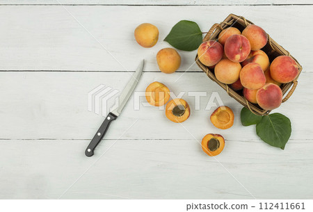 Ripe apricots and apricot leaves in a bowl on a wooden table. Fresh fruits from the home garden Ripe apricots and apricot leaves in a bowl on a wooden table. Fresh fruits from the home garden 112411661