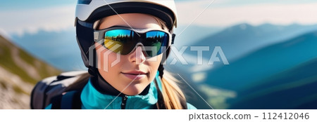 Woman wearing helmet and sunglasses glasses stands confidently before towering mountain backdrop ready for adventure, exploration.She may be gearing up for bicycle ride or some other outdoor activity. Woman wearing helmet and sunglasses glasses stands confidently before towering mountain backdrop ready for adventure, exploration.She may be gearing up for bicycle ride or some other outdoor activity. 112412046